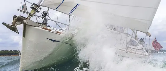 Segelyacht in Welle - Skipper-Absicherung Eine Segelyacht fährt durch eine Welle mit Gischt.