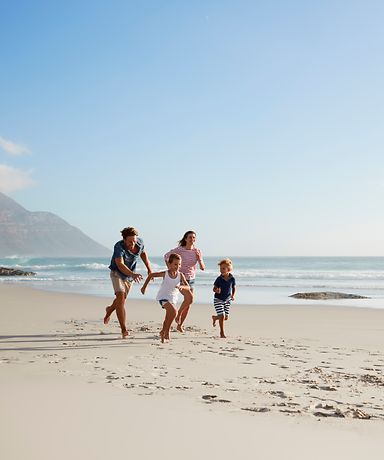 Eine Familie läuft am Strand. Im Hintergrund kann man das Wasser und einen Berg sehen.