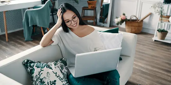 Eine Frau sitzt in ihrer Wohnung am Laptop und lächelt. 