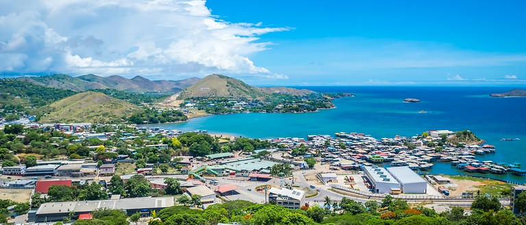 Man erkennt eine kleine Stadt in Papua-Neuguinea von oben. Im Hintergrund sieht man Wasser.