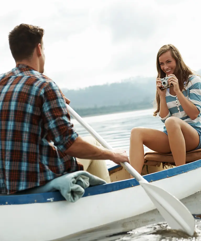 Ein Mann und eine Frau sitzen auf einem Ruderboot. Die Frau hält eine Kamera in der Hand und lächelt. 