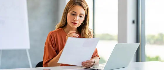 Eine Frau sitzt mit Papieren am Schreibtisch vor ihrem Laptop