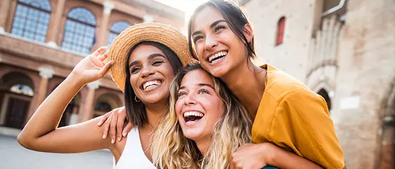 Junge Menschen am Lachen - Reiseversicherung für Schüler & Studenten Verschieden Personen sitzen an einem Tisch und lachen. Auf dem Tisch kann man Laptops sehen.