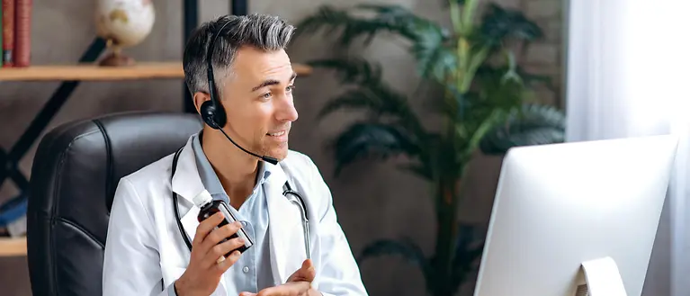 Ein Arzt sitzt mit Headset vor einem Monitor