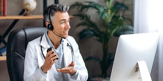 A doctor is sitting in front of a monitor wearing a headset