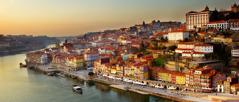 Man sieht einen Hügel mit der Altstadt von Porto. Im Vordergrund ist ein Fluss zu sehen.
