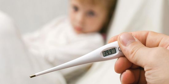 Im Vordergrund erkennt man ein weißes Fieberthermometer. Im Hintergrund ist verschwommen ein kleines Kind zu erkennen. 
