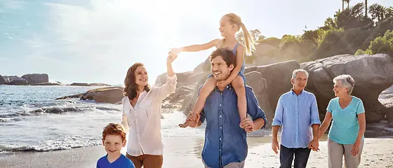 Mutter, Vater und deren Tochter gehen gemeinsam mit Oma und Opa am Strand spazieren.
