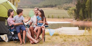 Mutter, Vater und ihre Kinder sitzen vor einem Zelt. Im Hintergrund ist Wasser zu sehen. 