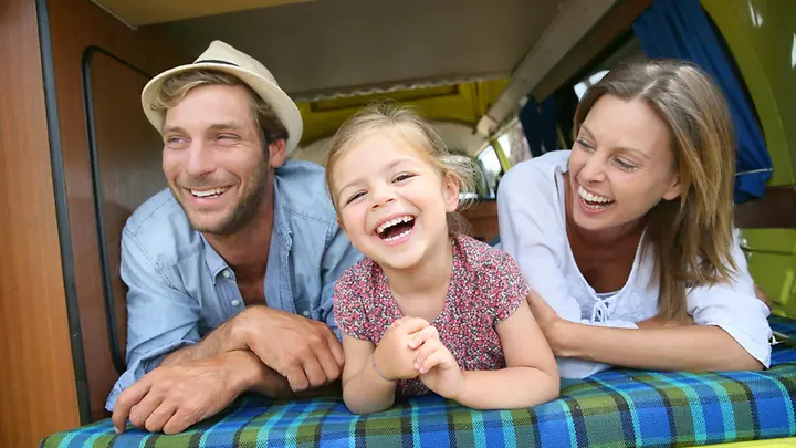 Familie im Camper - Camping-Urlaub Mutter, Vater und ihre Tochter liegen in einem Camper und lachen.
