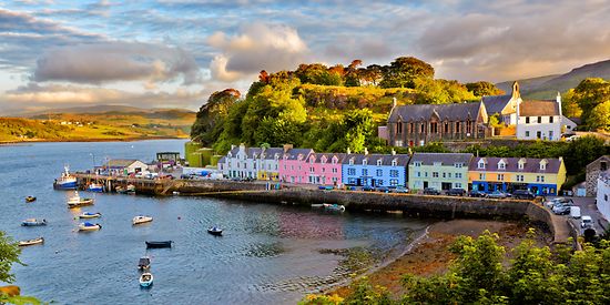 Man sieht eine kleine Stadt auf der Isle of Skye. Die Häuser sind bunt und stehen in einer Bucht am Wasser. 