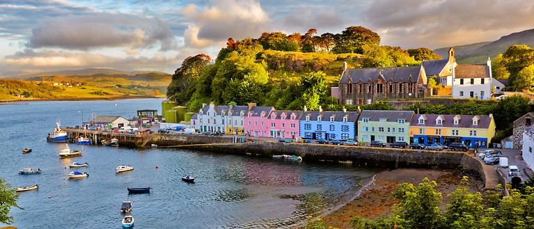 Man sieht eine kleine Stadt auf der Isle of Skye. Die Häuser sind bunt und stehen in einer Bucht am Wasser. 
