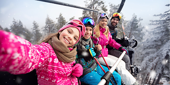 Eine Familie sitzt in einem Skilift und machen ein Selfie. 