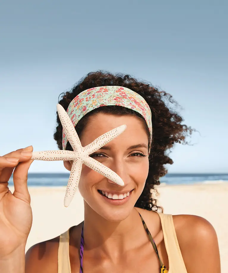 Eine Frau steht am Strand mit einem Seestern in der Hand.
