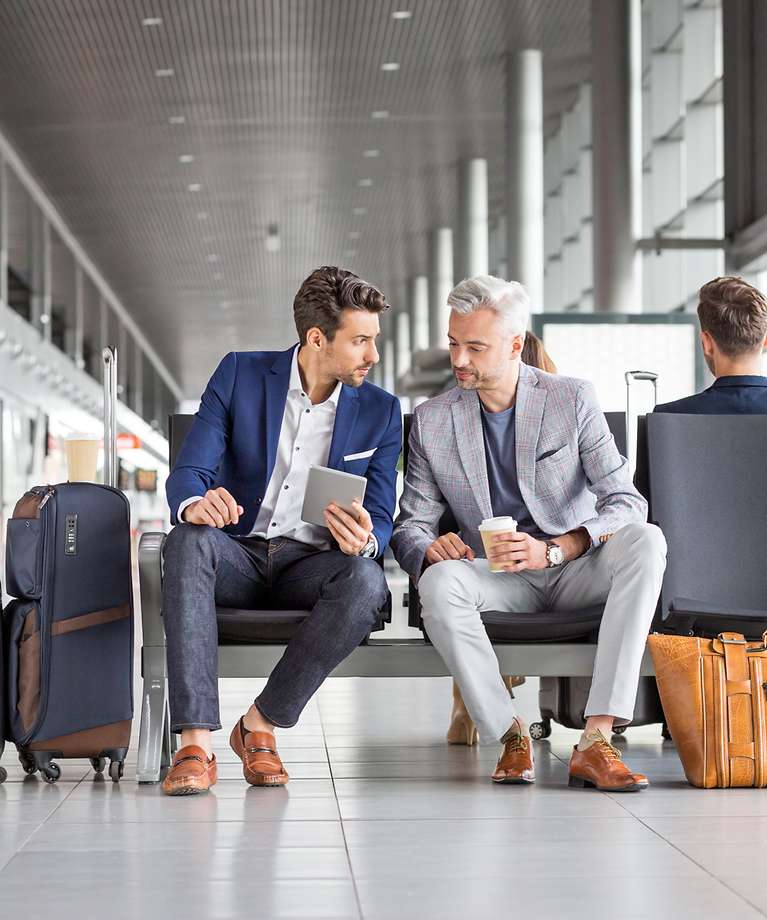 Zwei Männer sitzen am Flughafen und besprechen sich.