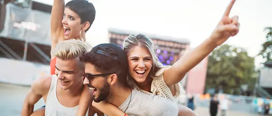 Vier Freunde - Ticketversicherung Vier Freunde sind auf einem Konzert. Die Jungs tragen die Mädchen Huckepack.