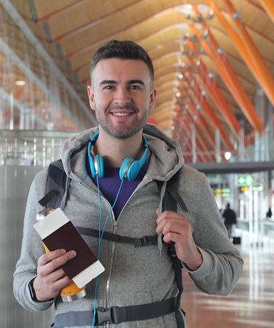 Ein Mann steht mit einem Reisepass in der Hand am Flughafen.