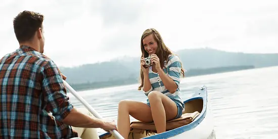 Ein Mann und eine Frau sitzen auf einem Ruderboot. Die Frau hält eine Kamera in der Hand und lächelt. 