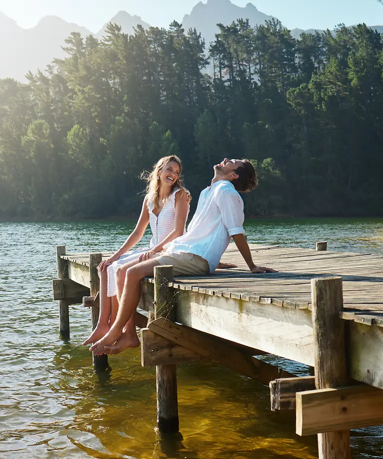 Ein Mann und eine Frau sitzen auf einem Steg, der ins Wasser hineinführt und lachen.