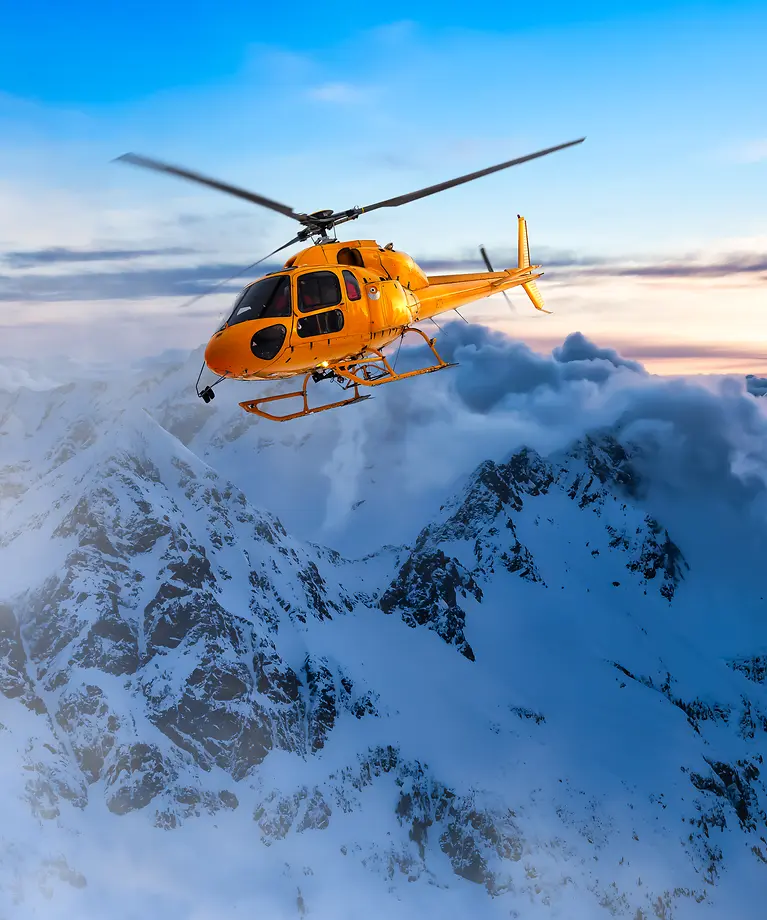 Ein gelber Helikopter fliegt bei Sonnenuntergang über die Rocky Mountains